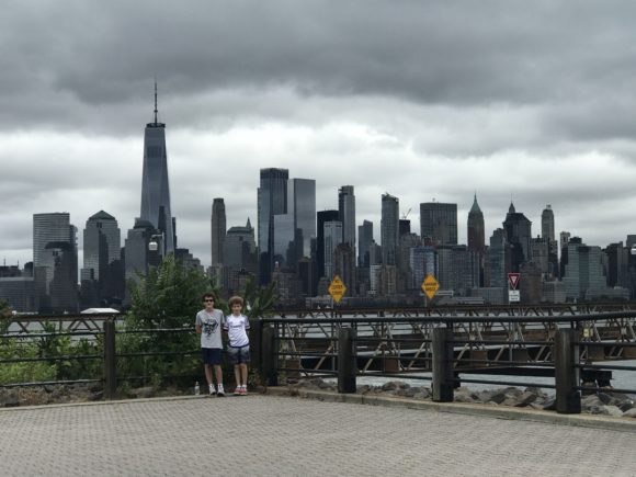 boys stand on hudson river waterfront walkway with Manhattan skyline in the distance