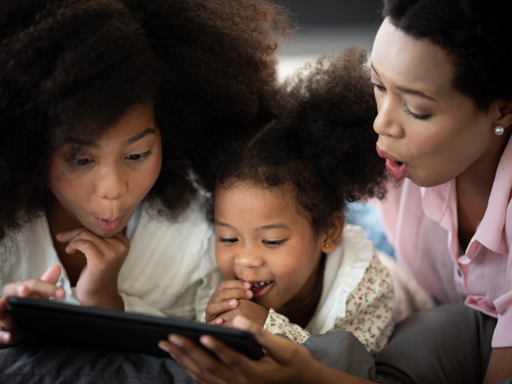 African American mother watches movies on a tablet with 2 daughters