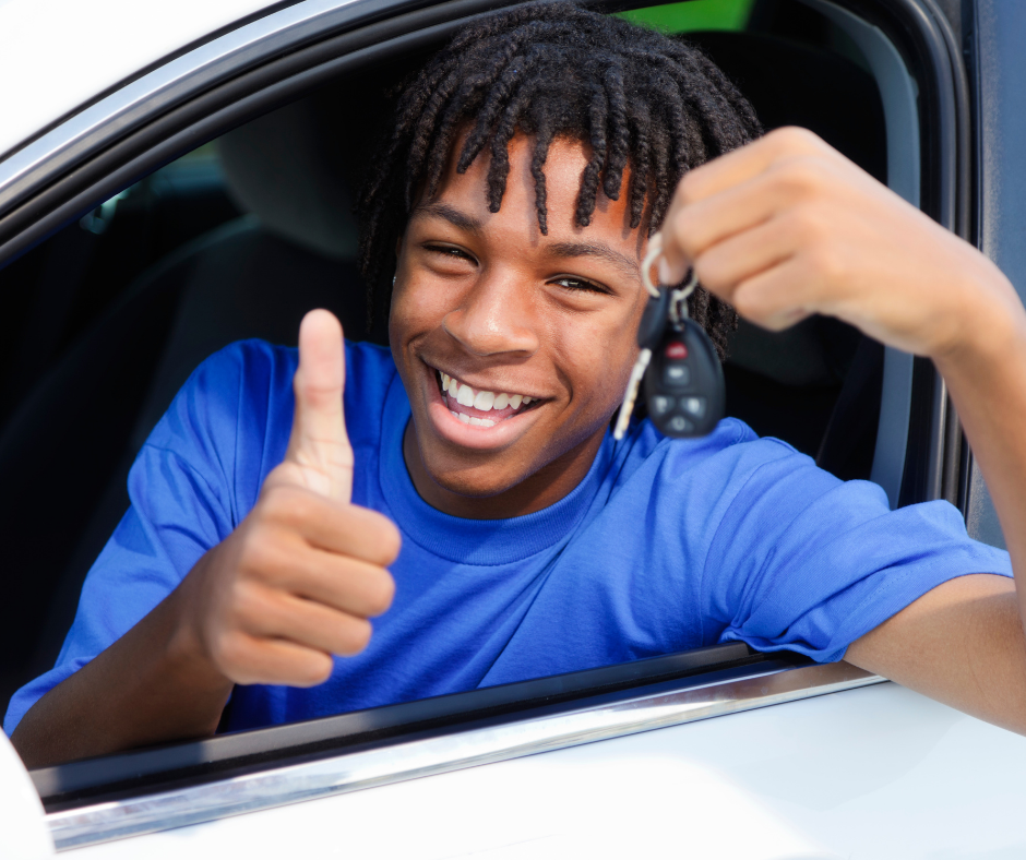 black male teenager sits in a car giving a thumbs up and holding a set of keys.