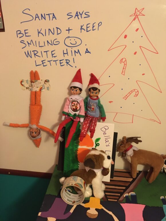 A group of elves write a message on a dry erase board.
