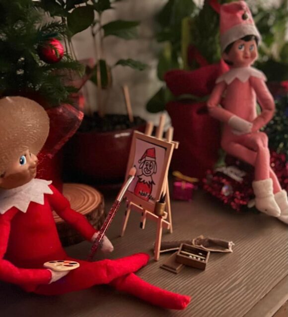 An elf on the shelf paints a picture of another elf on the shelf