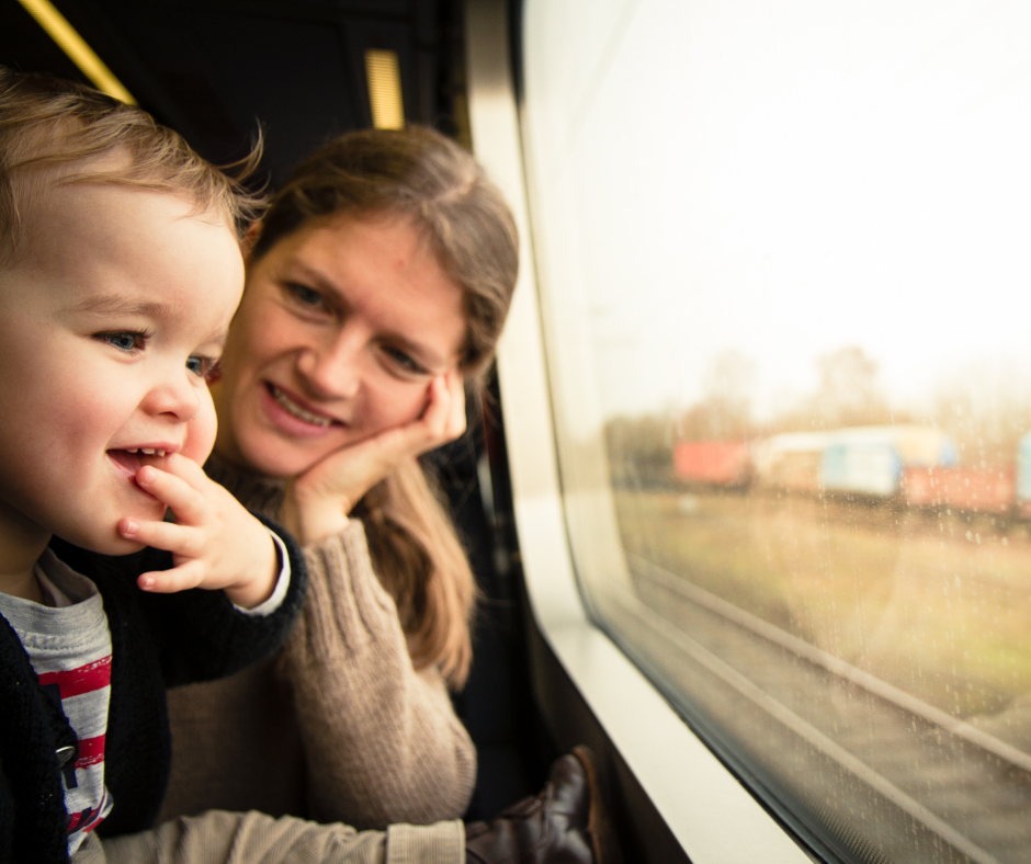 child and adult looks out the window of a passenger car on a train